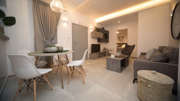 Uma sala de estar moderna com área de jantar, sofá, televisão e uma planta decorativa.