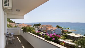 A balcony with a table and chairs, overlooking a coastal town with houses and the sea. - Apartment Topic near Beach (Podstrana)