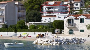 A coastal building with multiple balconies, a sandy beach, and a boat in the water. - Apartment Topic near Beach (Podstrana)