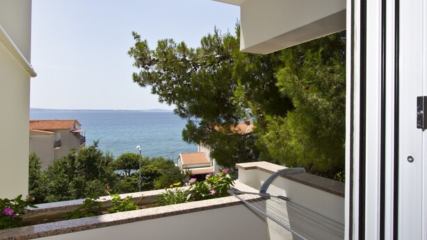 A balcony with a view of the sea and a building with a tiled roof. - Apartment Topic near Beach (Podstrana)