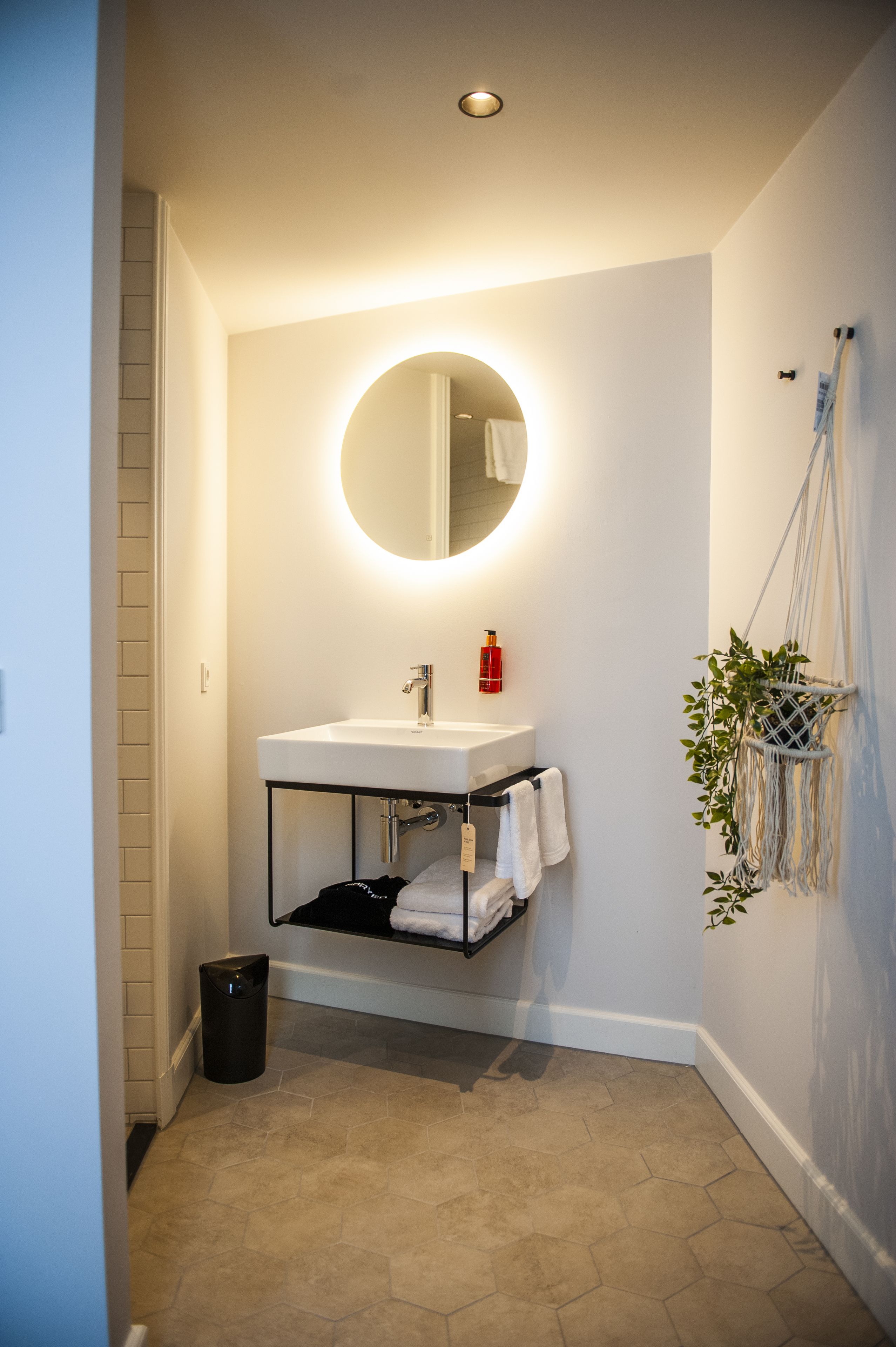 Een badkamer met een witte wastafel, een ronde spiegel en een handdoekhouder.