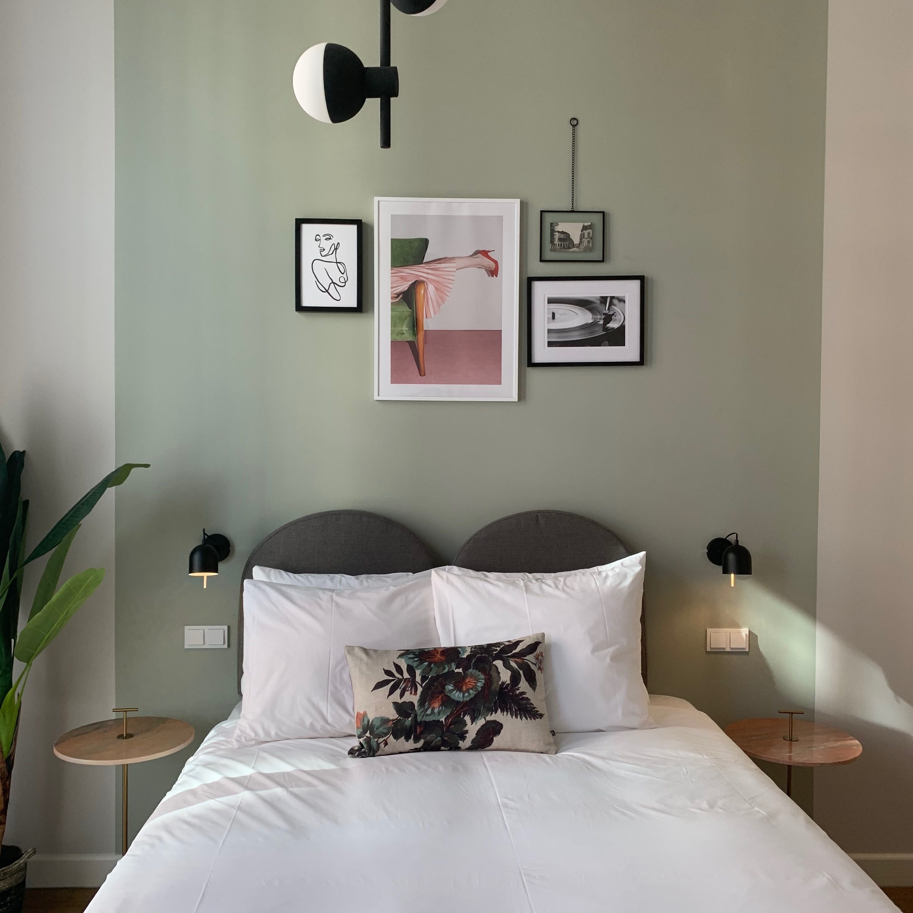 A bedroom with a bed, two bedside tables, a wall-mounted lamp, and framed artwork.