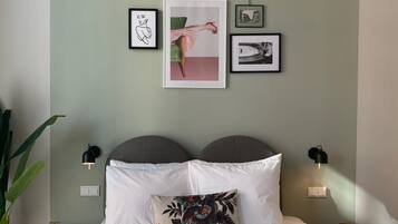 A bedroom with a bed, two bedside tables, a wall-mounted lamp, and framed artwork.