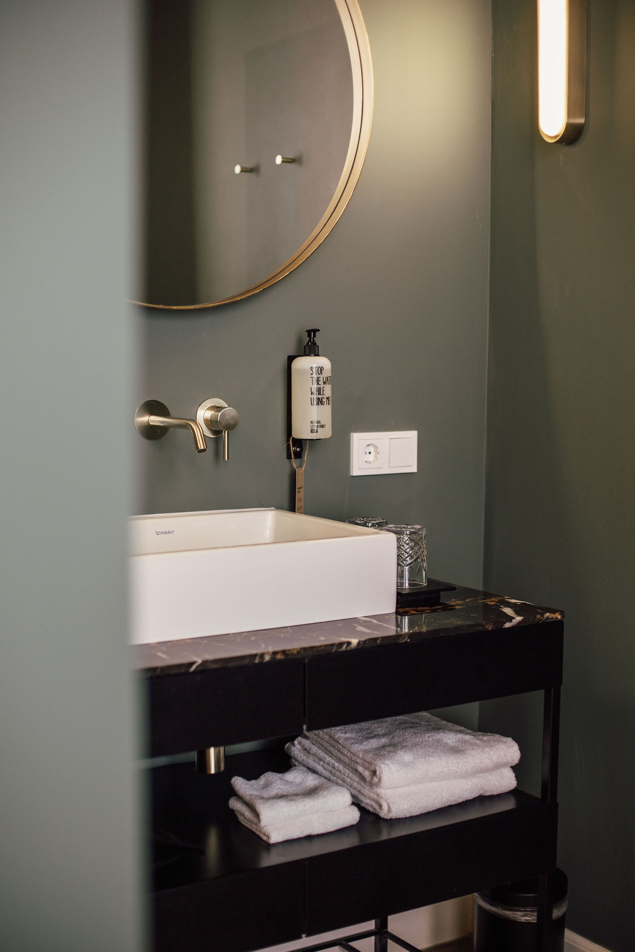 Un baño con lavamanos blanco, tocador negro, espejo y perchero.