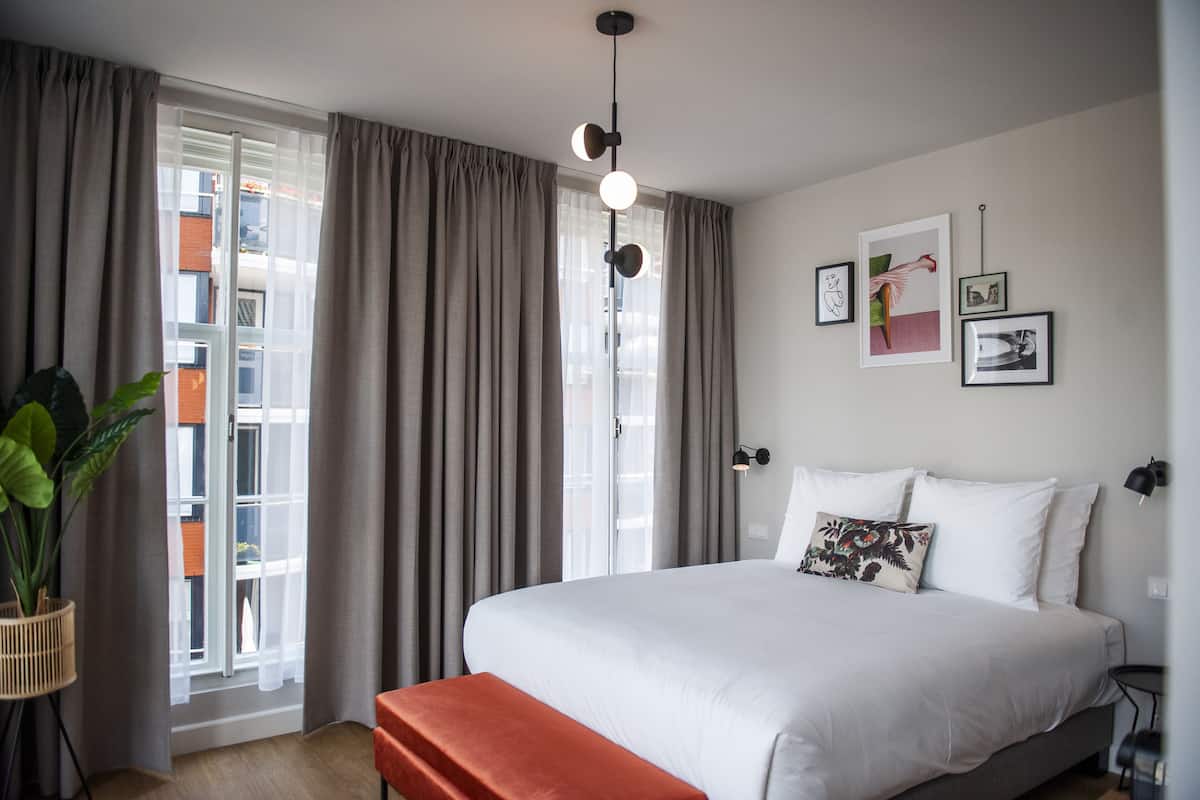 A bedroom with a bed, a bench, a potted plant, and a window with curtains.