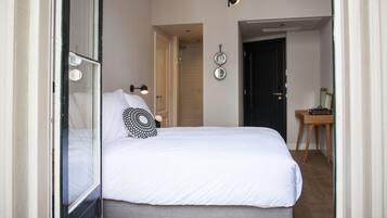 Een slaapkamer met een groot bed, een nachtkastje, een spiegel en een deur naar een andere kamer.