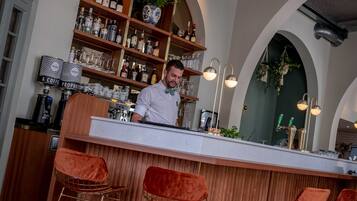 Una zona de bar con un cantinero, estantes de madera con botellas y una barra moderna.