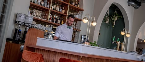 Un espace bar avec un barman, des étagères en bois remplies de bouteilles et un comptoir de bar moderne.