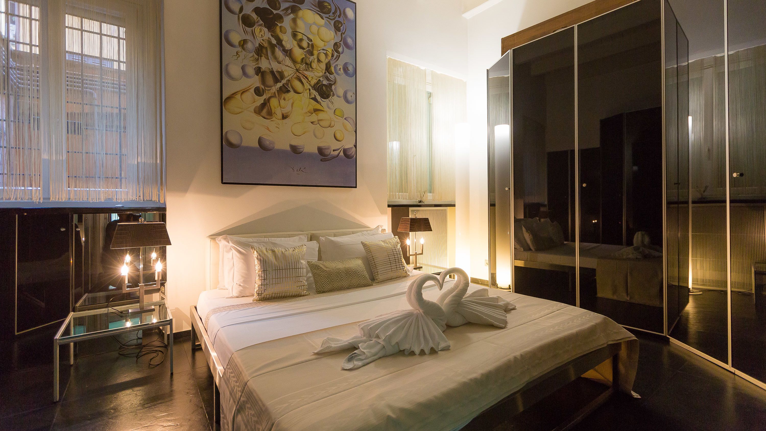 A modern hotel room with a large bed, a glass partition, and a painting on the wall.