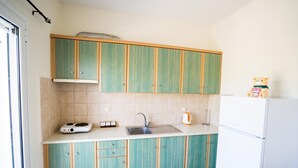 A compact kitchen with teal cabinets, a white countertop, a sink, a kettle, and a refrigerator. - Denise Apartments (Zakynthos)
