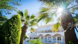 A two-story building with a white facade, multiple balconies, and a stone-paved courtyard. - Denise Apartments (Zakynthos)