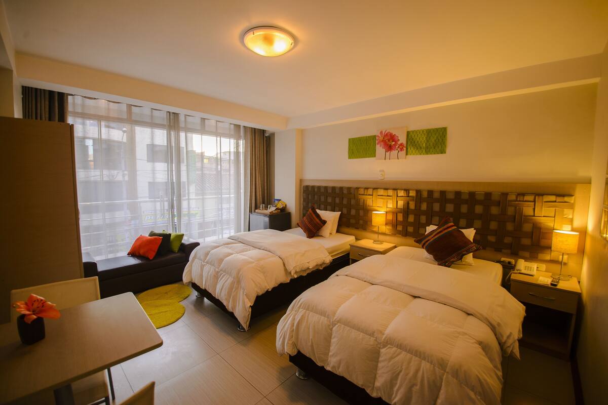 Ein Hotelzimmer mit zwei Betten, einem Schreibtisch und einem fenster mit Vorhängen.