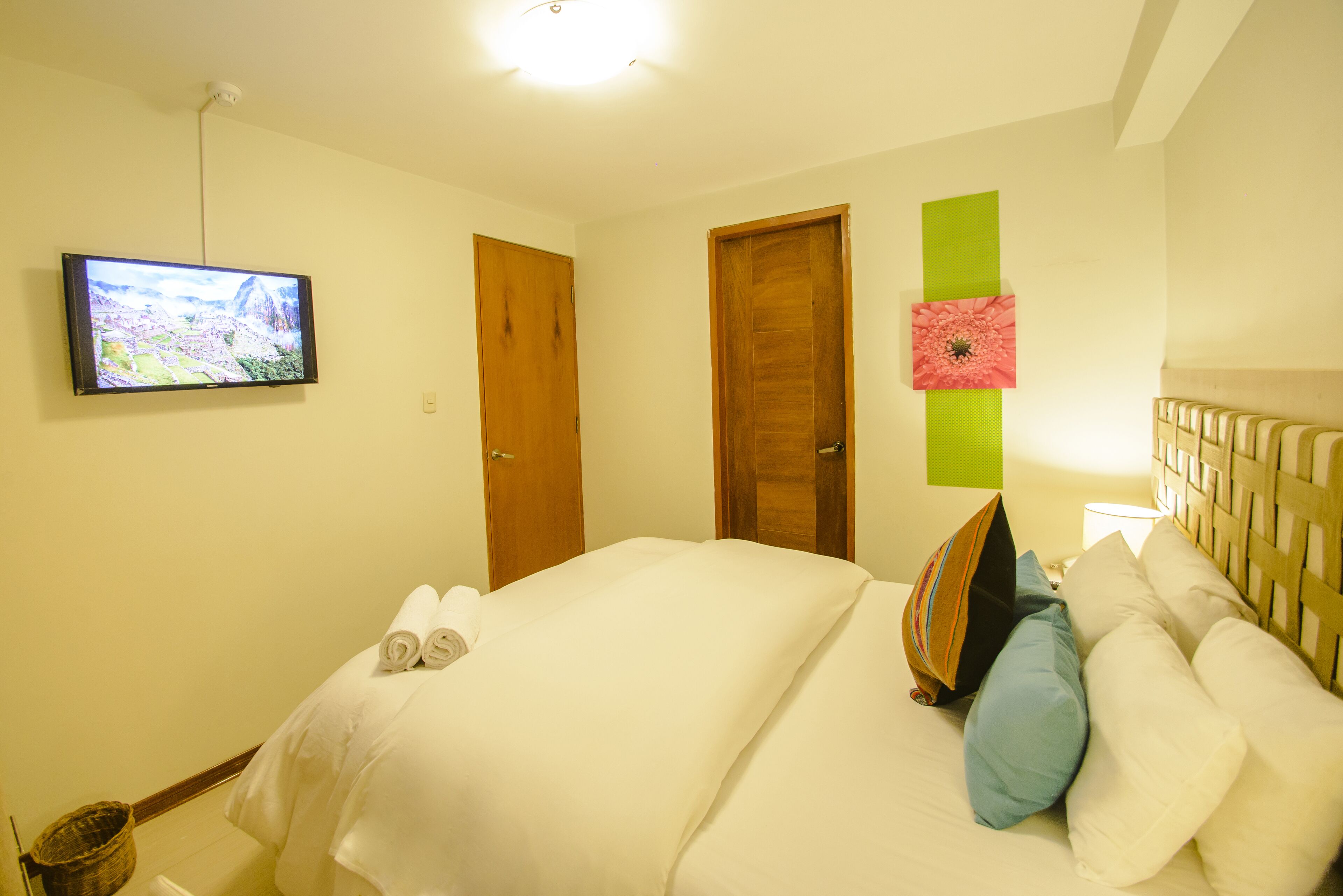 Una habitación de hotel con cama, televisión en la pared y dos puertas.