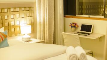 Habitación de hotel con una cama, una mesita de noche con lámpara, un ordenador portátil sobre una pequeña mesa y una ventana con cortinas.