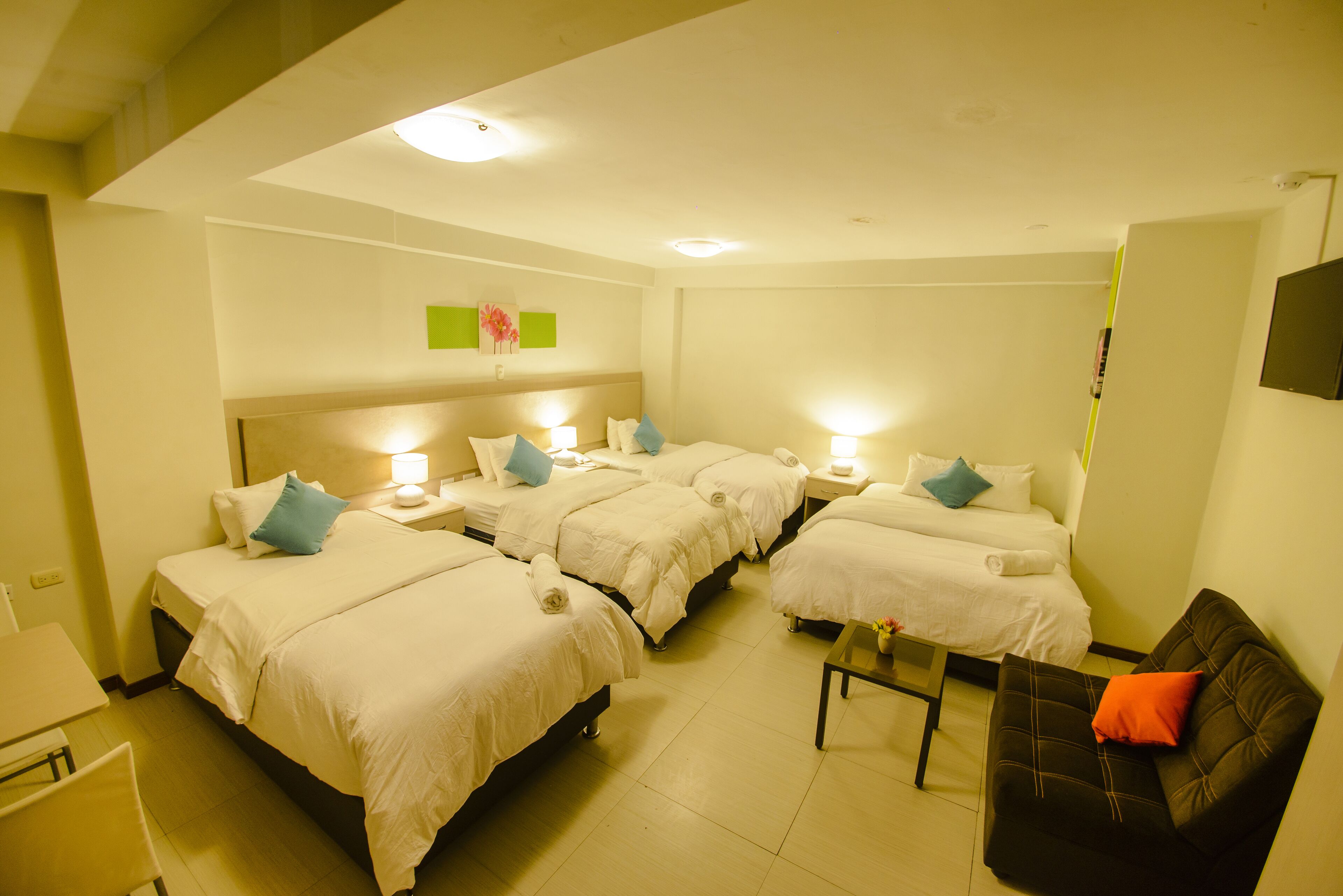 A hotel room with four beds, a sofa, a table, and a TV.