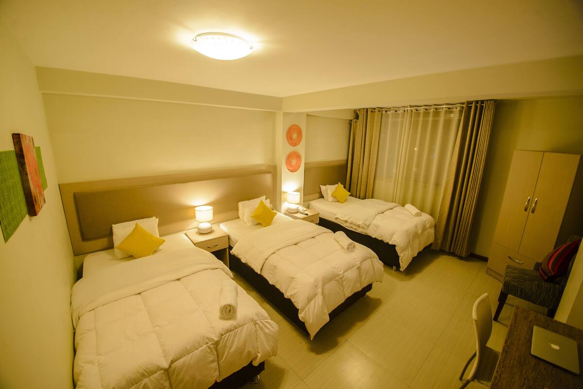 Ein Hotelzimmer mit drei Betten, einem Schreibtisch und einem Stuhl.
