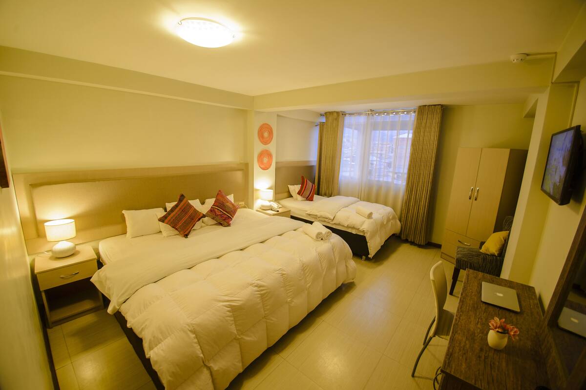 Ein Hotelzimmer mit zwei Betten, einem Schreibtisch mit einem Laptop, einem Stuhl, einem Kleiderschrank und einem an der Wand befestigten Fernseher.