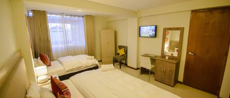 Quarto de hotel com duas camas, uma escrivaninha, uma cadeira, uma televisão e um guarda-roupa.