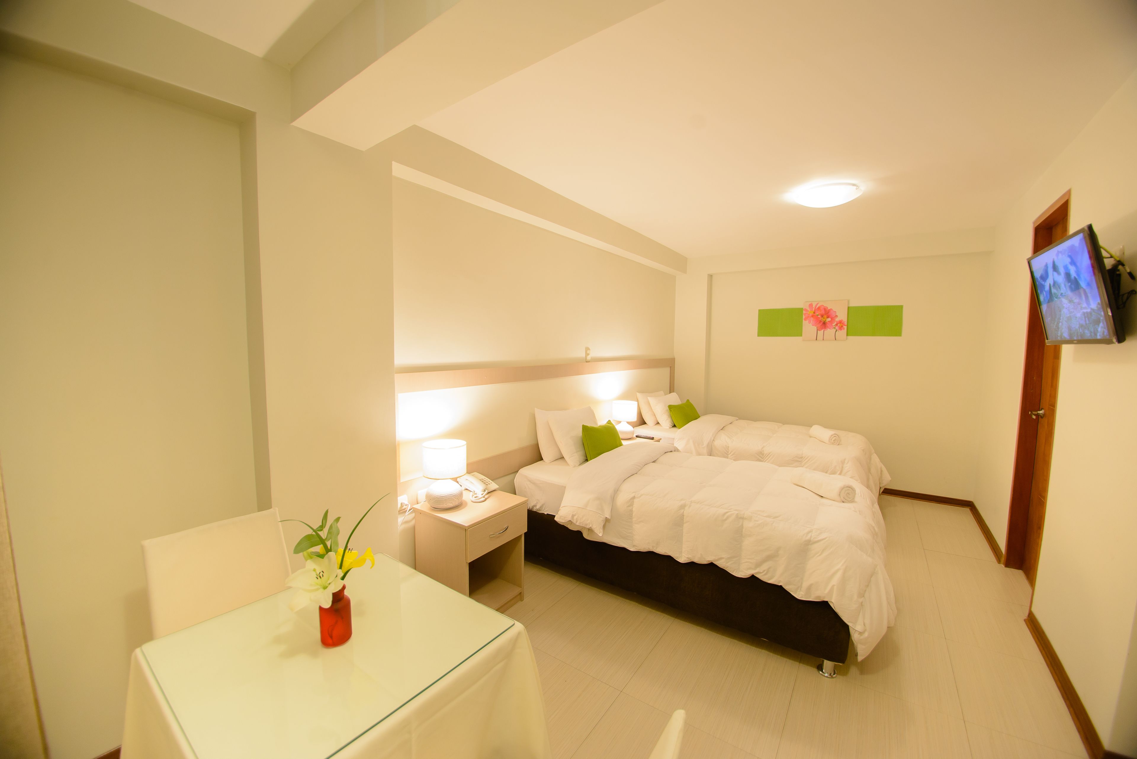 Una habitació d'hotel amb llit, una taula de nit, una làmpada i una taula petita amb un vas de flors.