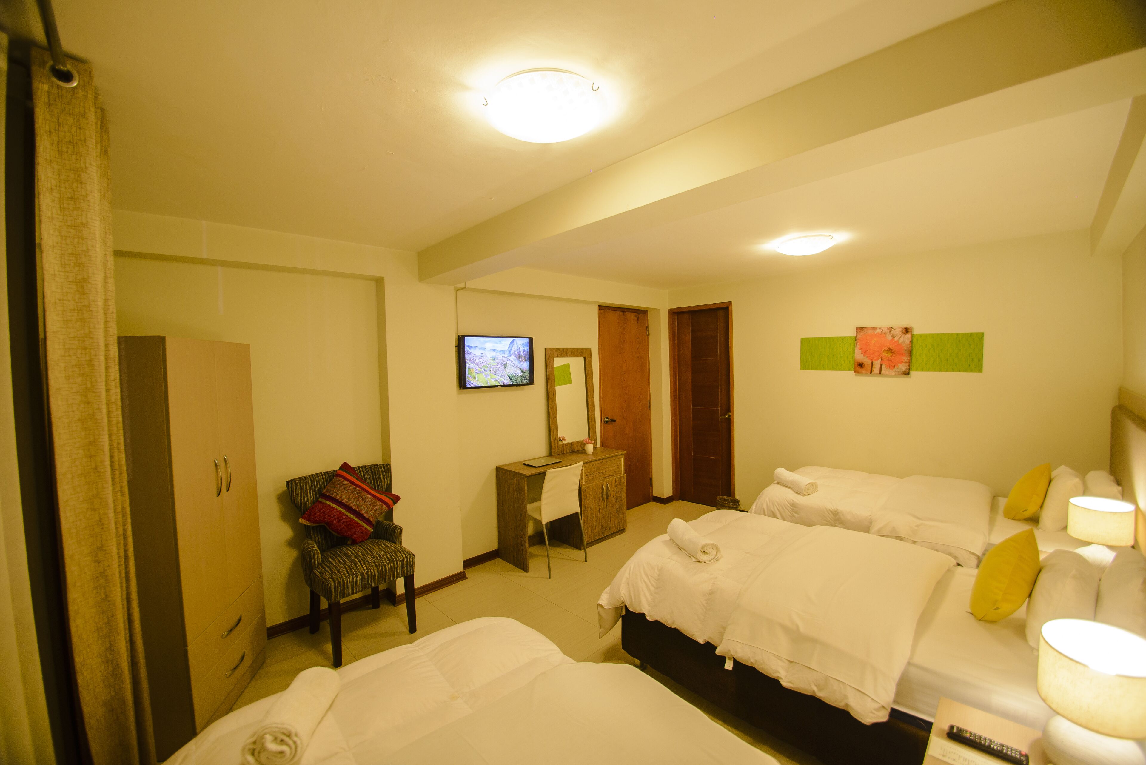 A hotel room with two beds, a desk, a chair, a wardrobe, and a television.