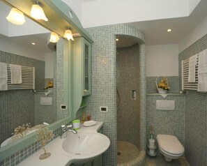 A bathroom with a sink, mirror, shower, and toilet, featuring green mosaic tiles and white fixtures. - Casa Piva 1 (Val di Zoldo)