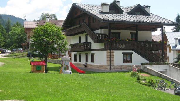 A two-story building with a balcony, a red slide, and a small playhouse. - Casa Piva 1 (Val di Zoldo)