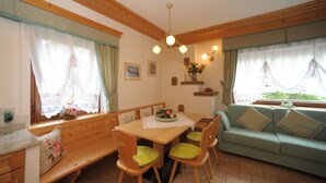 A cozy room with a wooden dining table, green cushioned chairs, a wooden bench, and a green sofa. - Casa Piva 1 (Val di Zoldo)