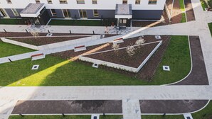 An aerial view of a courtyard with geometric pathways, a central garden, and a building with multiple windows and a sloped roof. - P&O Cybernetyki 7 (Warsaw)