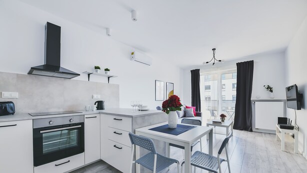 A modern kitchen with white cabinetry, a black oven, and a dining area with a table and chairs. - P&O Cybernetyki 7 (Warsaw)