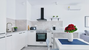 A modern kitchen with white cabinets, a built-in oven, a black range hood, and a dining area with a white table and blue placemat. - P&O Cybernetyki 7 (Warsaw)