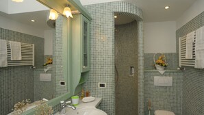 Casa de banho com lavatório, espelho, sanita e zona de duche, com azulejos de mosaico verde e toucador branco.