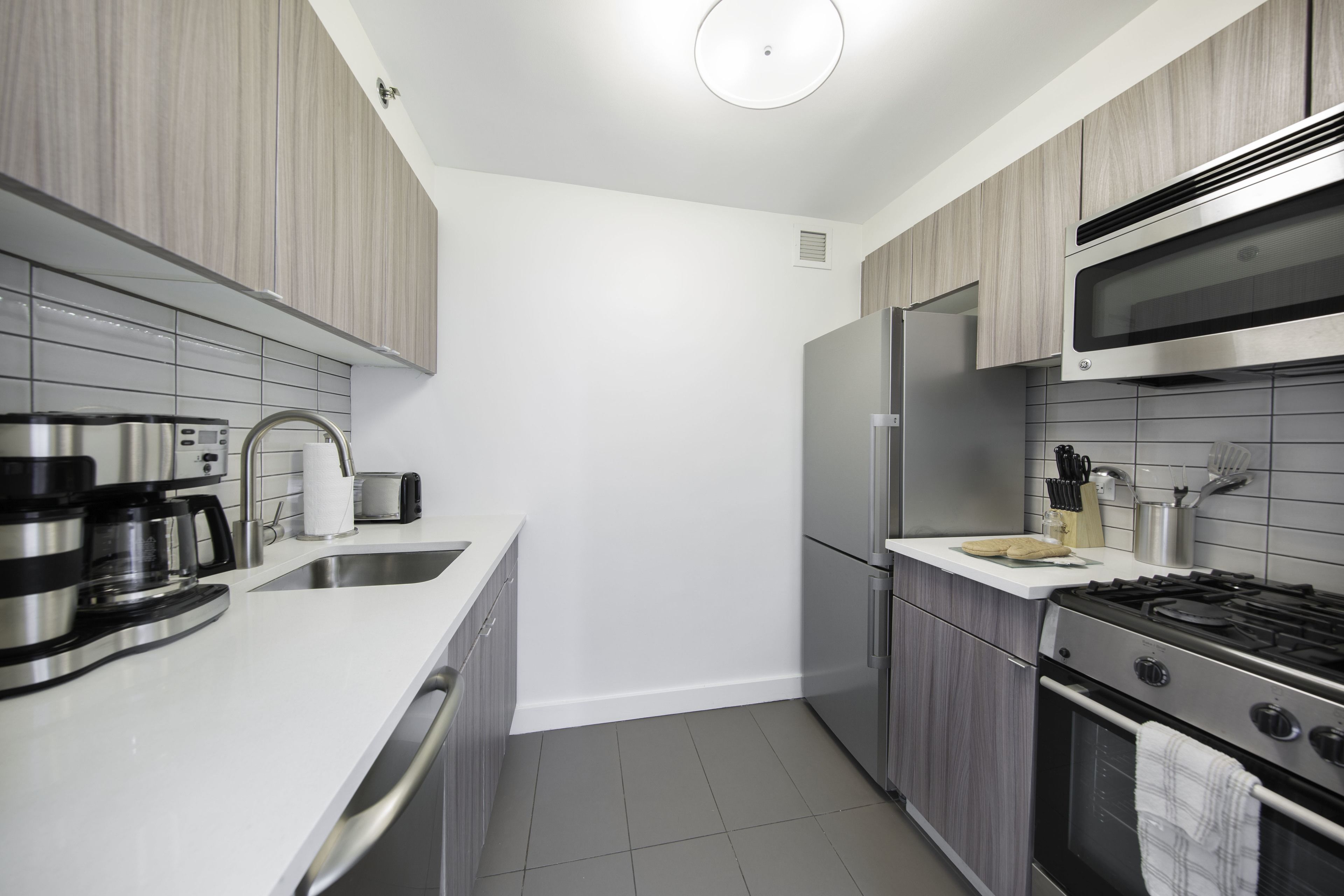 A modern kitchen with stainless steel appliances, a white countertop, and grey cabinetry.