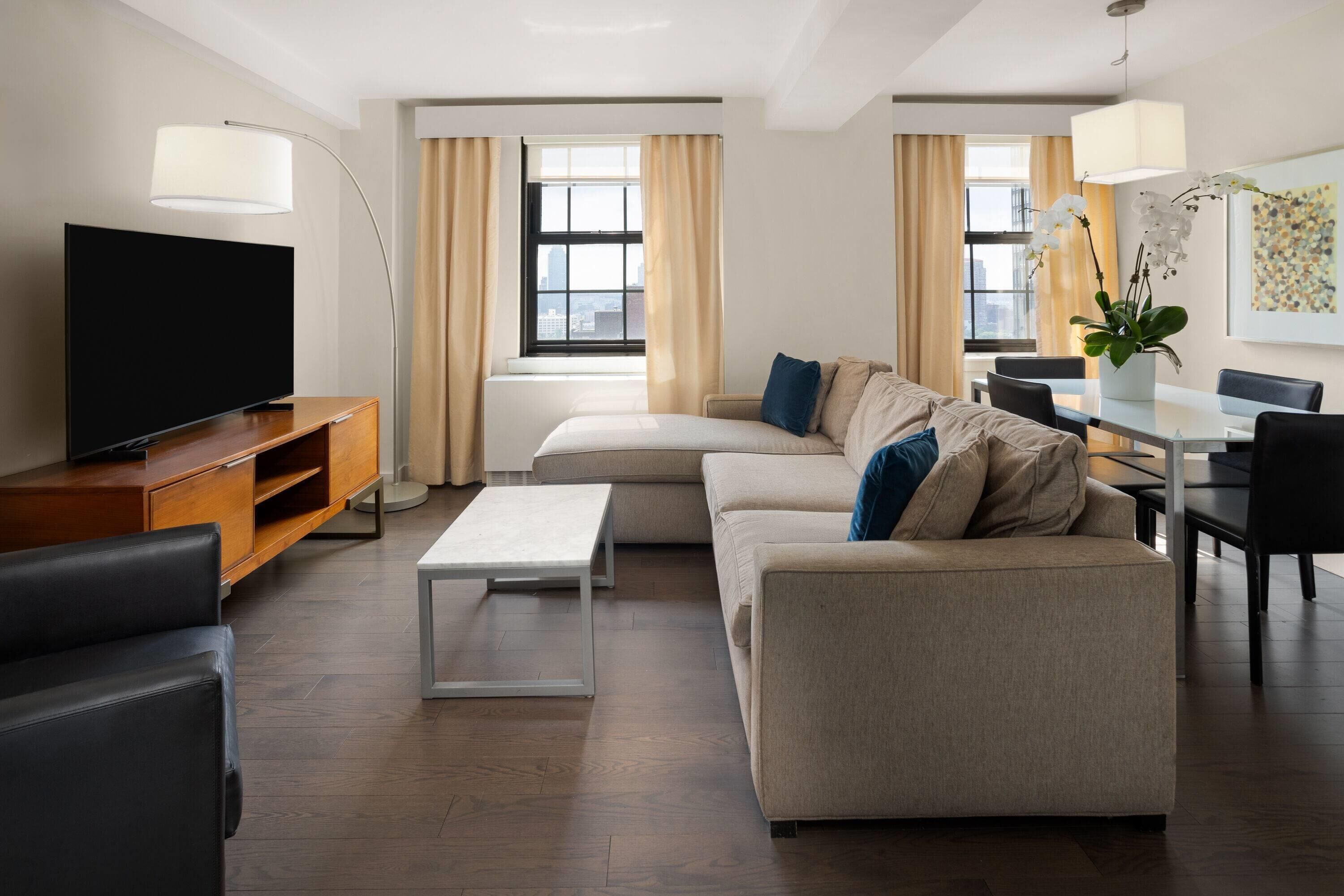 A modern living room with a flat-screen TV, a sofa, a coffee table, and a dining area with a table and chairs.