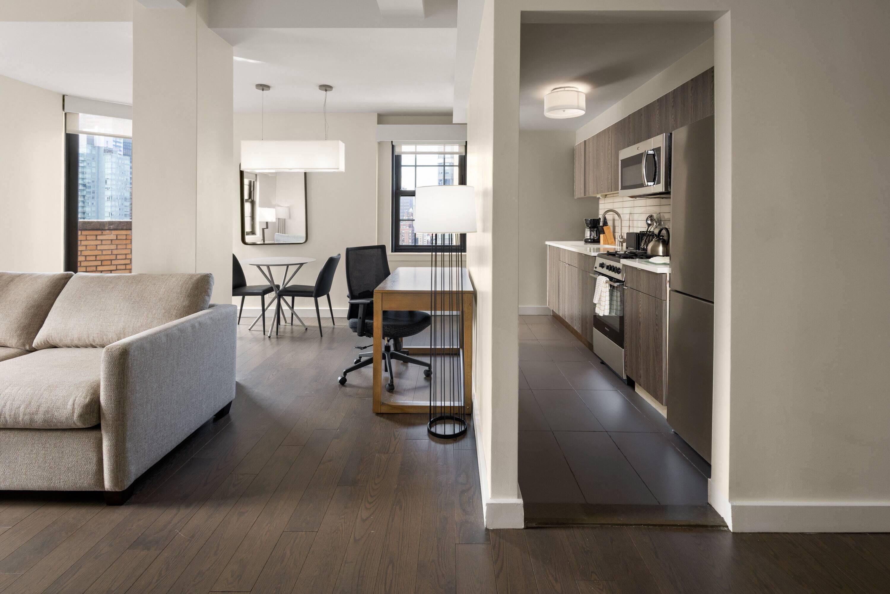 A modern living room with a sofa, a dining table with chairs, and a kitchen area with appliances.
