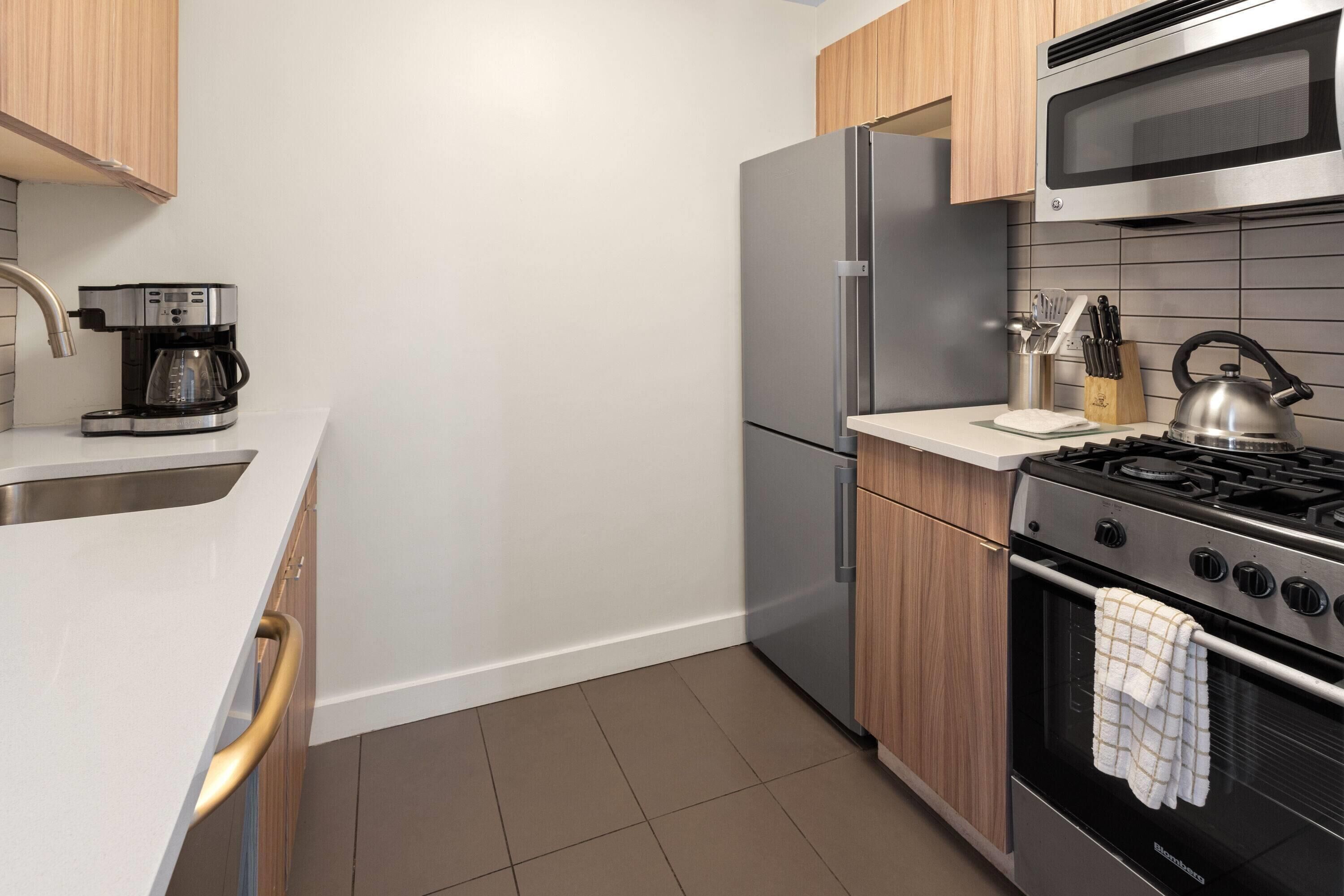 A modern kitchen with a stainless steel refrigerator, a built-in oven, a gas stove, and a coffee maker.