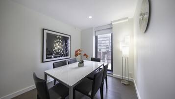 A modern dining area with a white table, black chairs, a vase with flowers, a framed abstract painting, and a floor lamp.