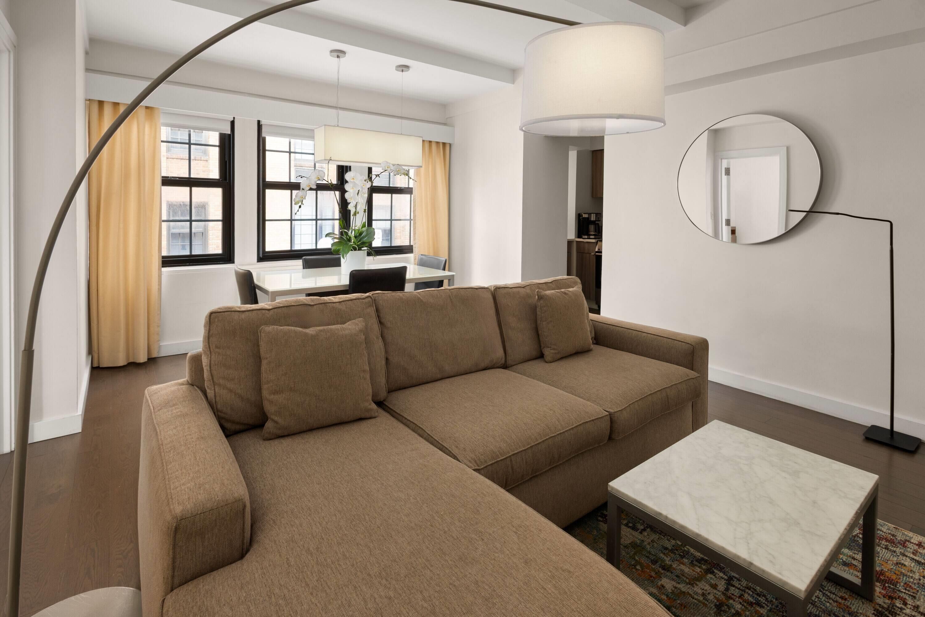 Un salon moderne avec un canapé d’angle, une petite table blanche et un miroir rond accroché au mur.