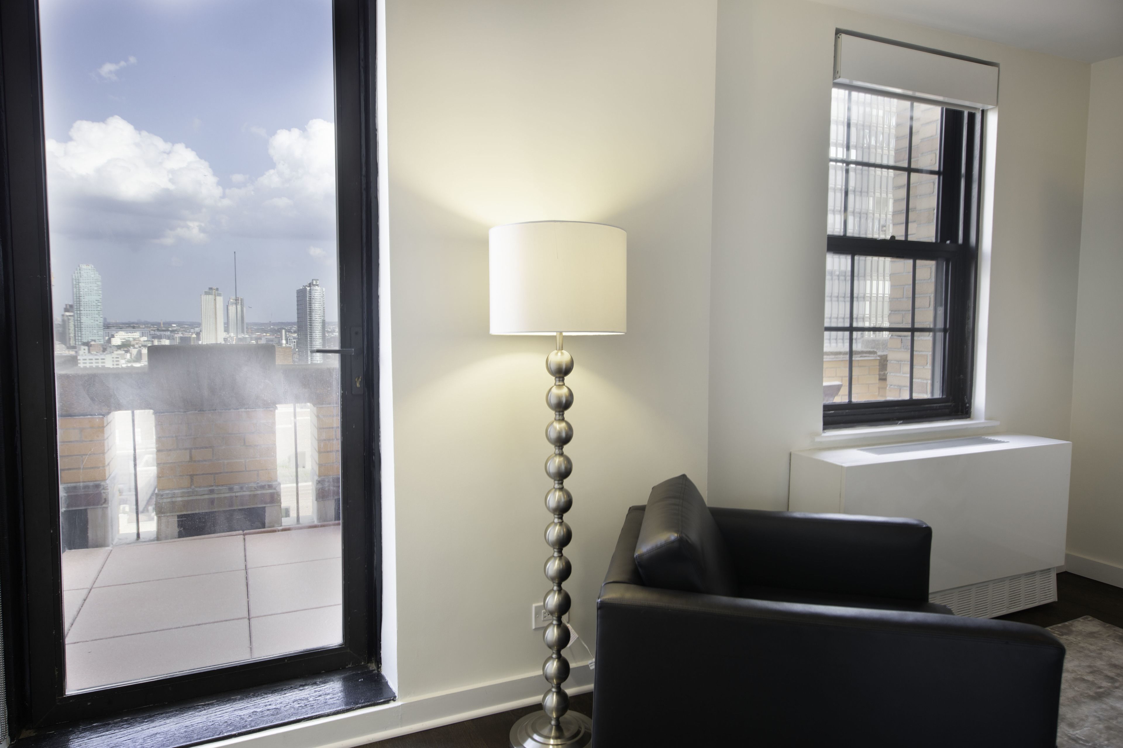 A room with a large window, a floor lamp, a radiator, and a black sofa.