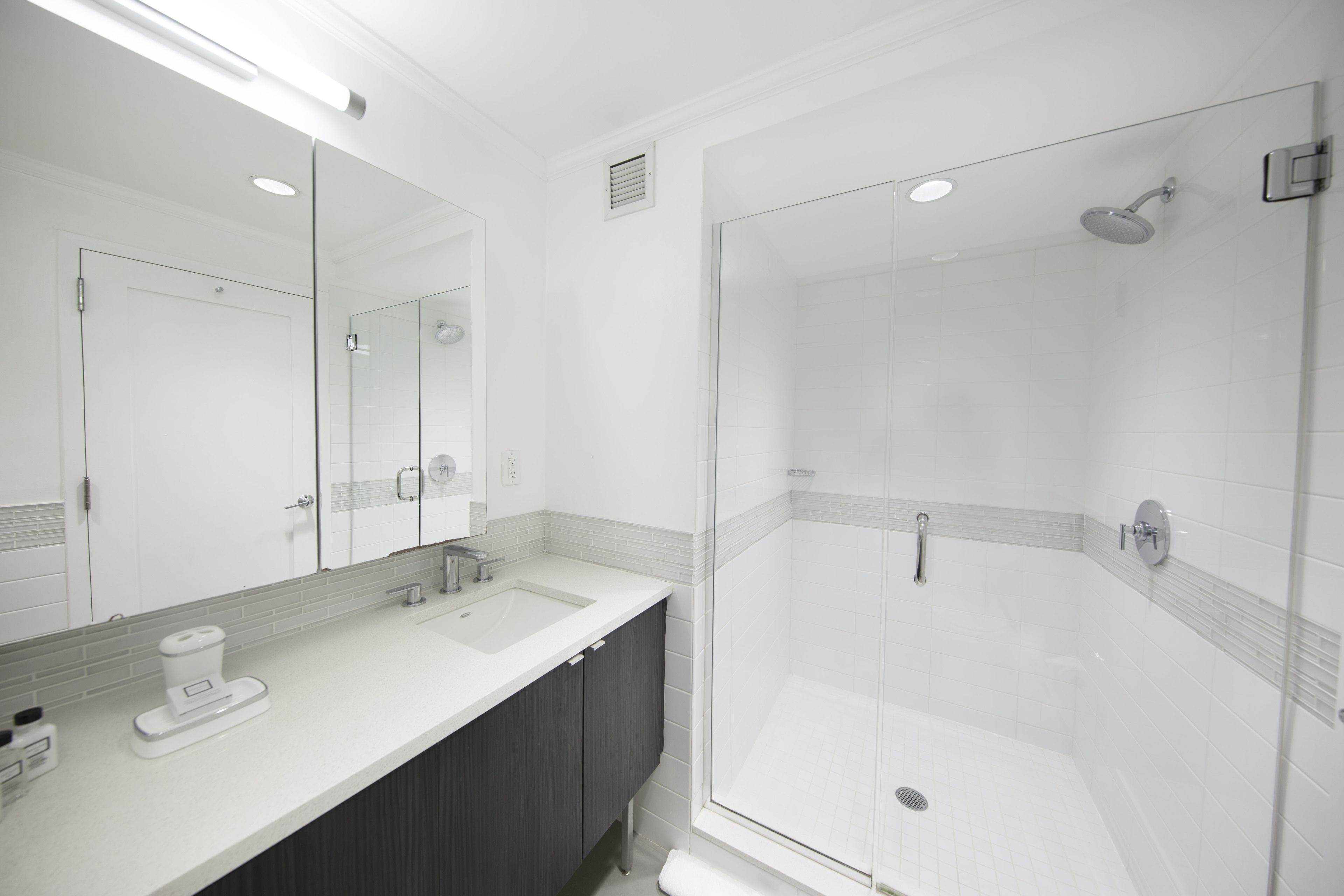 Un bagno moderno con doccia vetrata, uno specchio grande e un lavandino bianco.