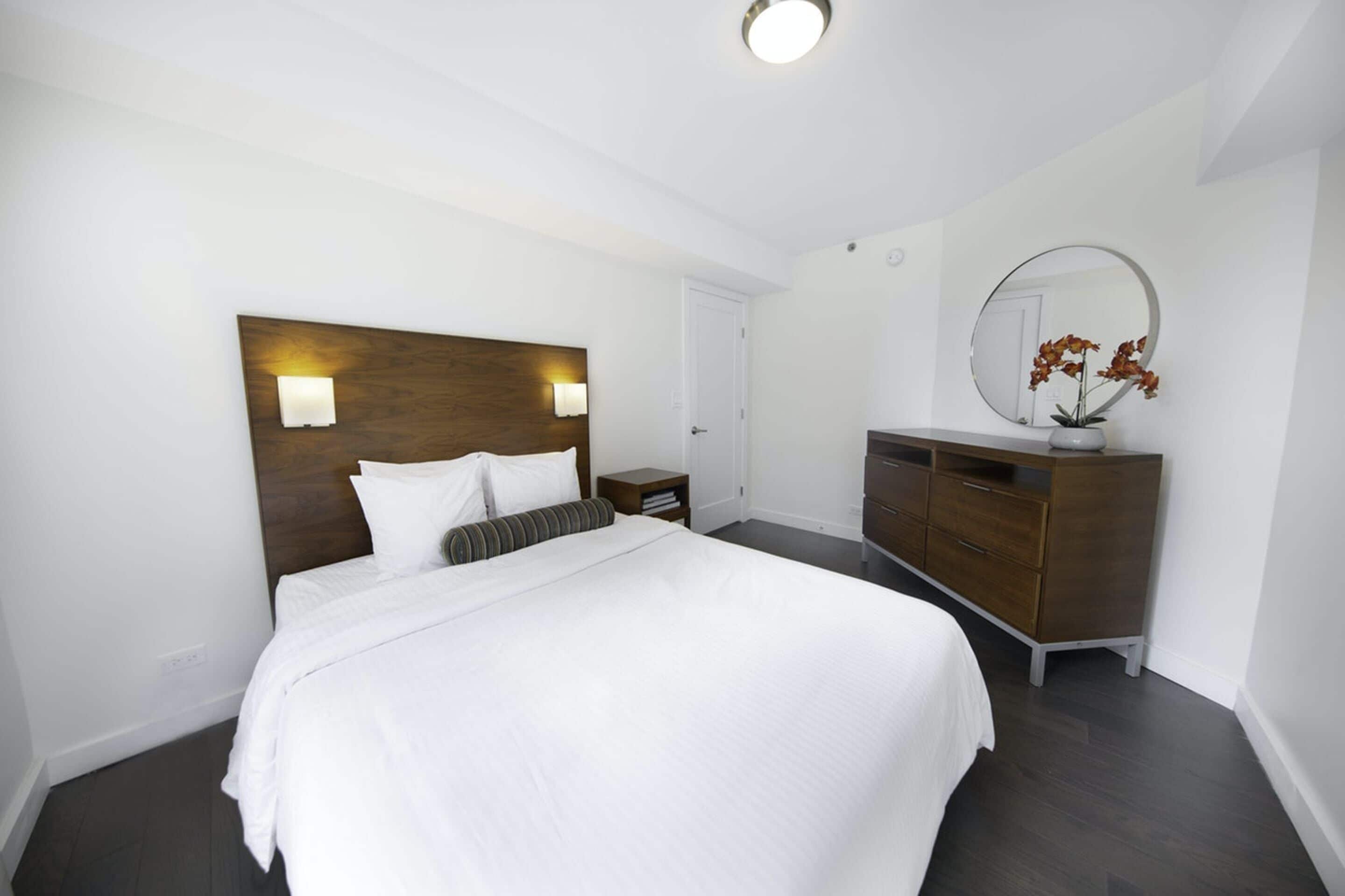 Une chambre d’hôtel avec un grand lit, une tête de lit en bois, des lampes de chevet, une commode et un miroir.