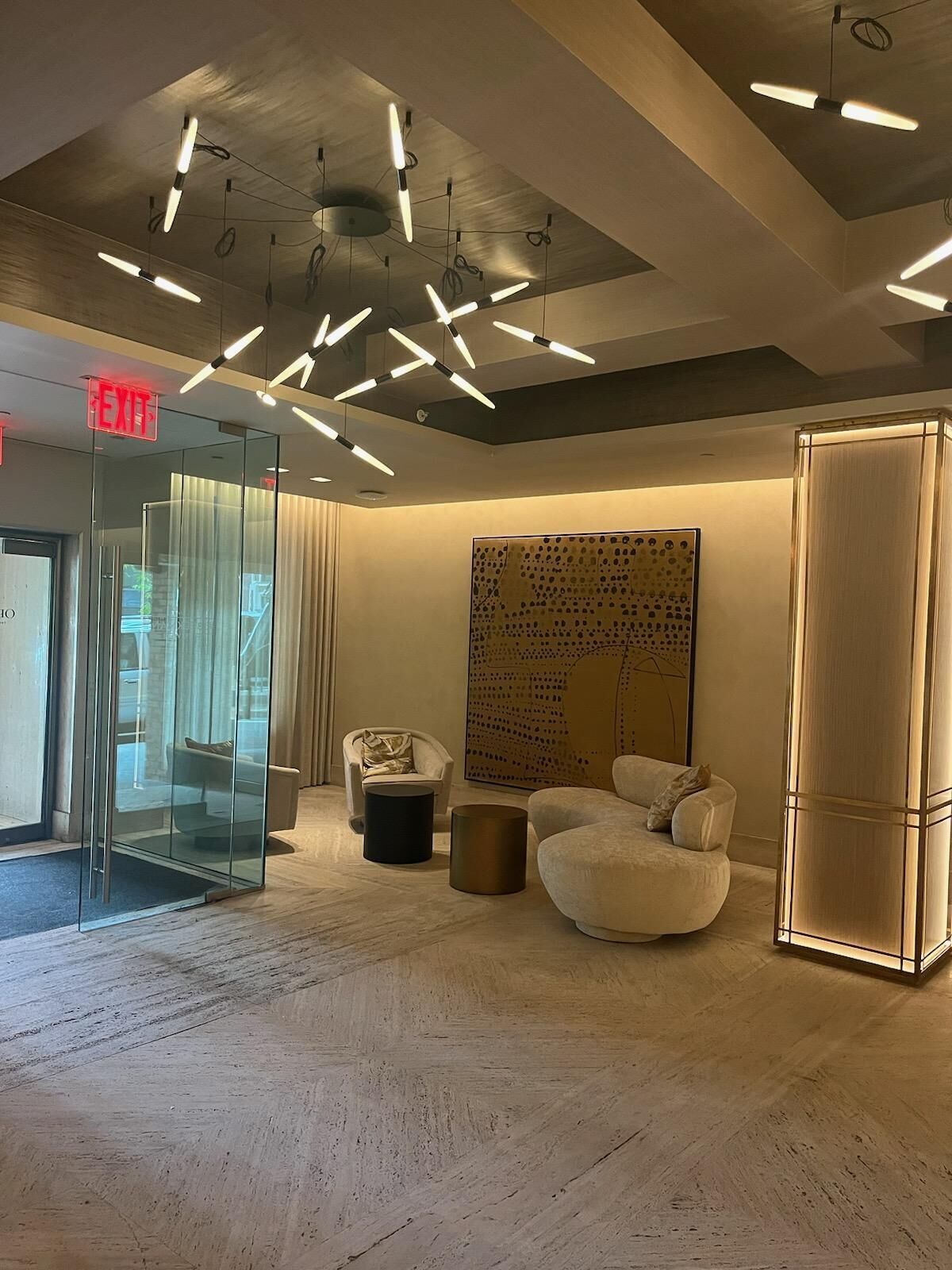 A modern lobby with a glass partition, a large abstract painting, and contemporary furniture.