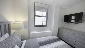 Een slaapkamer met een bed, nachtkastje, lamp, kapstok en een televisie.