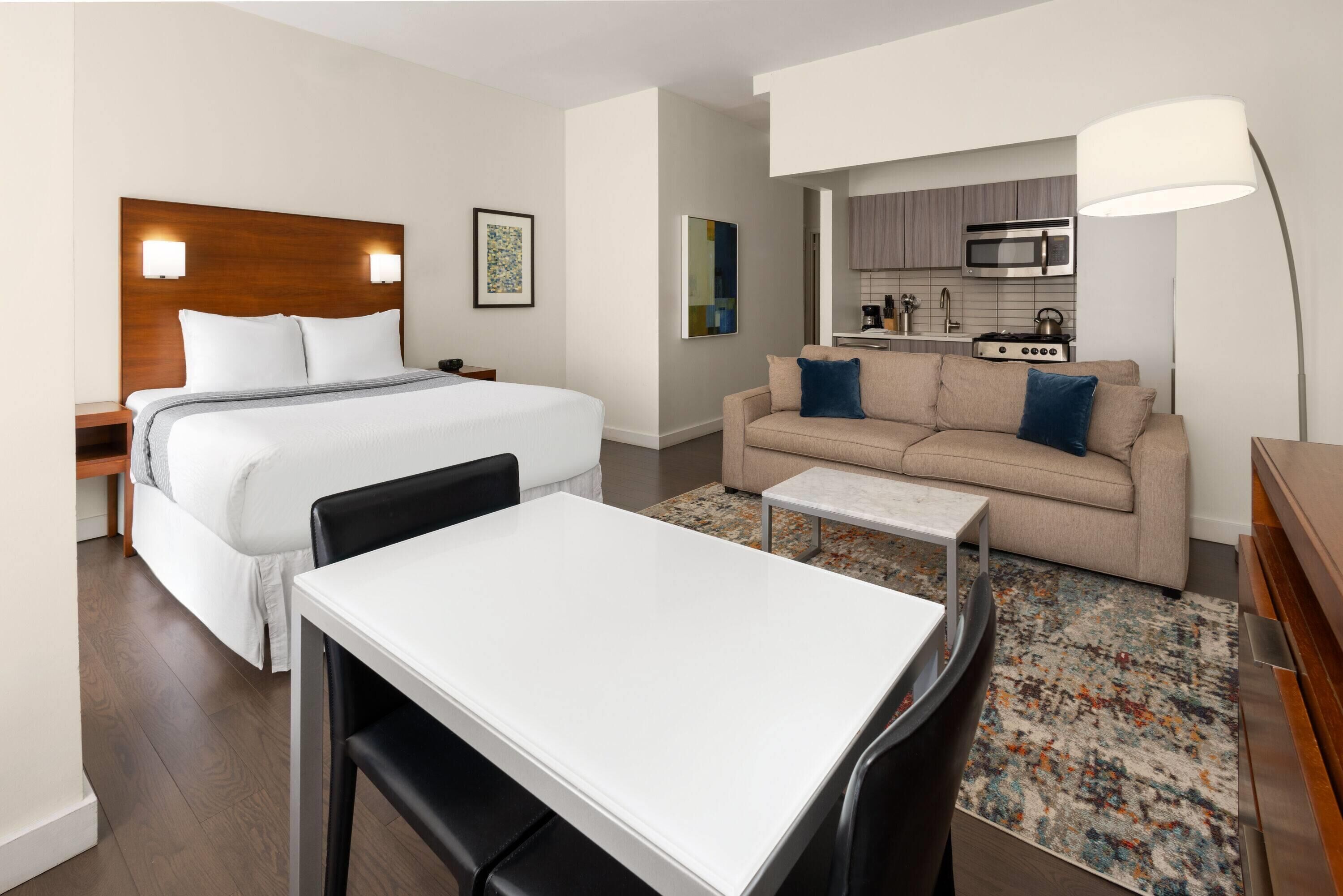 Een hotelkamer met een bed, een slaapbank, een tafeltje, een lamp en een kitchenette.