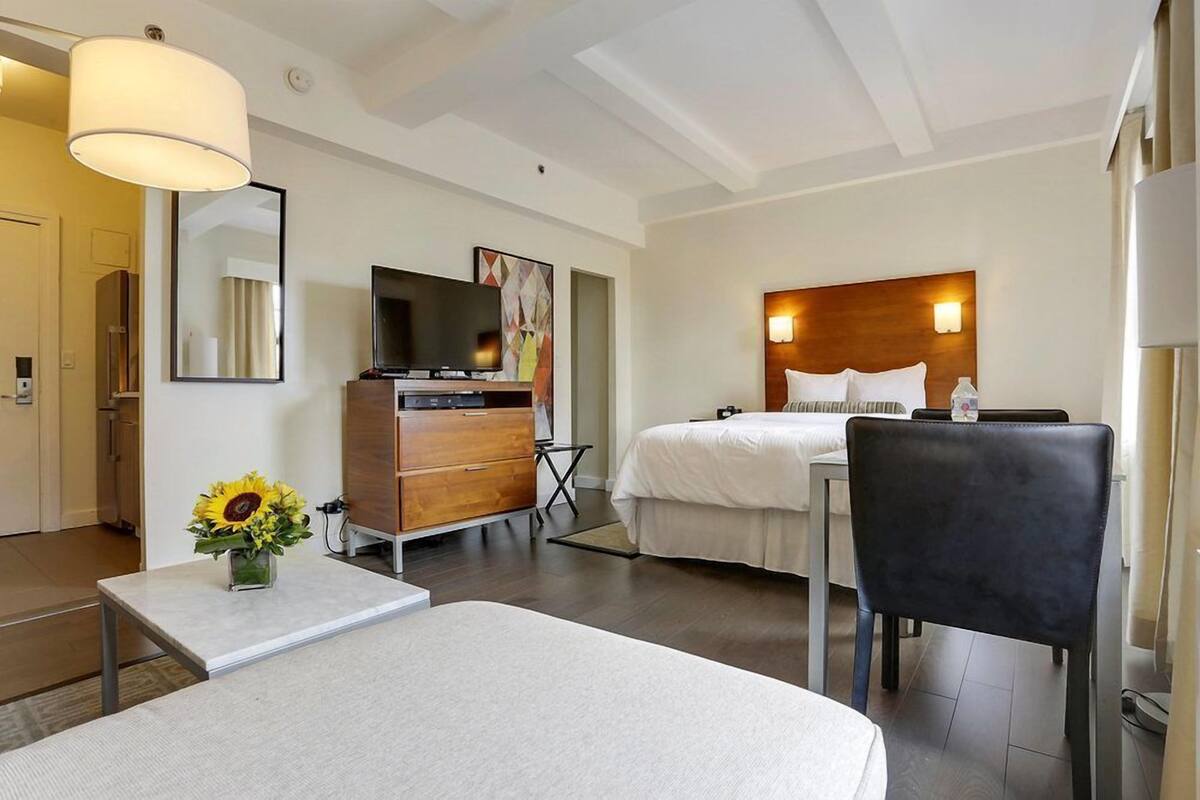 A hotel room with a bed, a desk, a dresser, a TV, and a large mirror.
