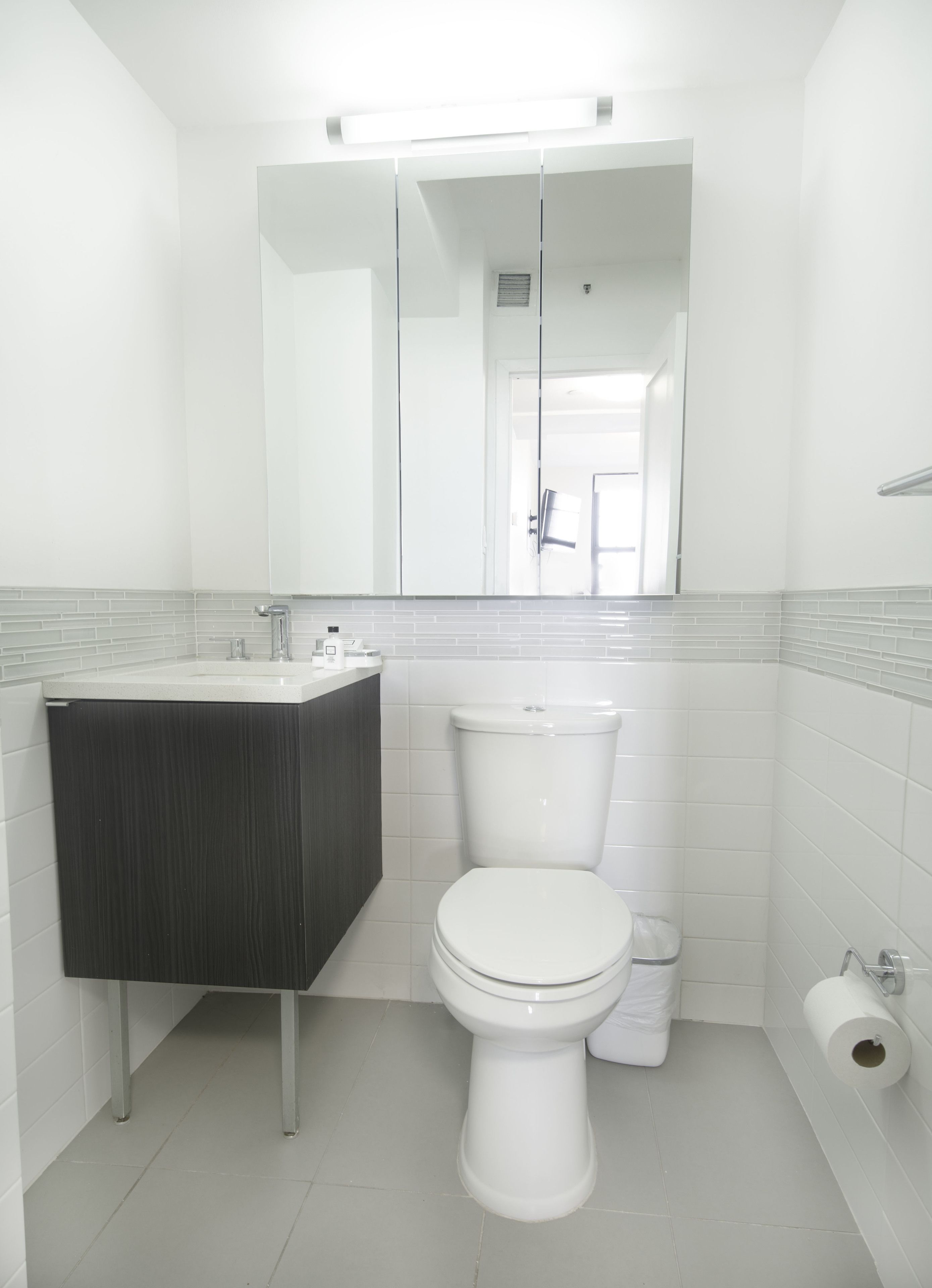 A modern bathroom with a white toilet, a dark-colored vanity, and a white sink.