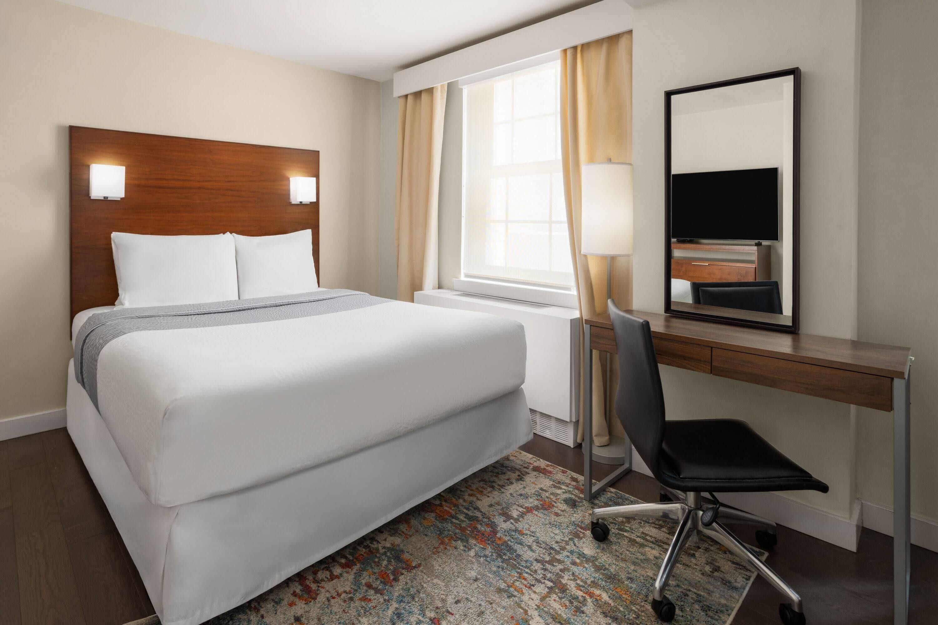 A hotel room with a large bed, a desk with a chair, a TV, and a window with curtains.
