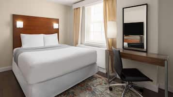 A hotel room with a large bed, a desk with a chair, a TV, and a window with curtains.