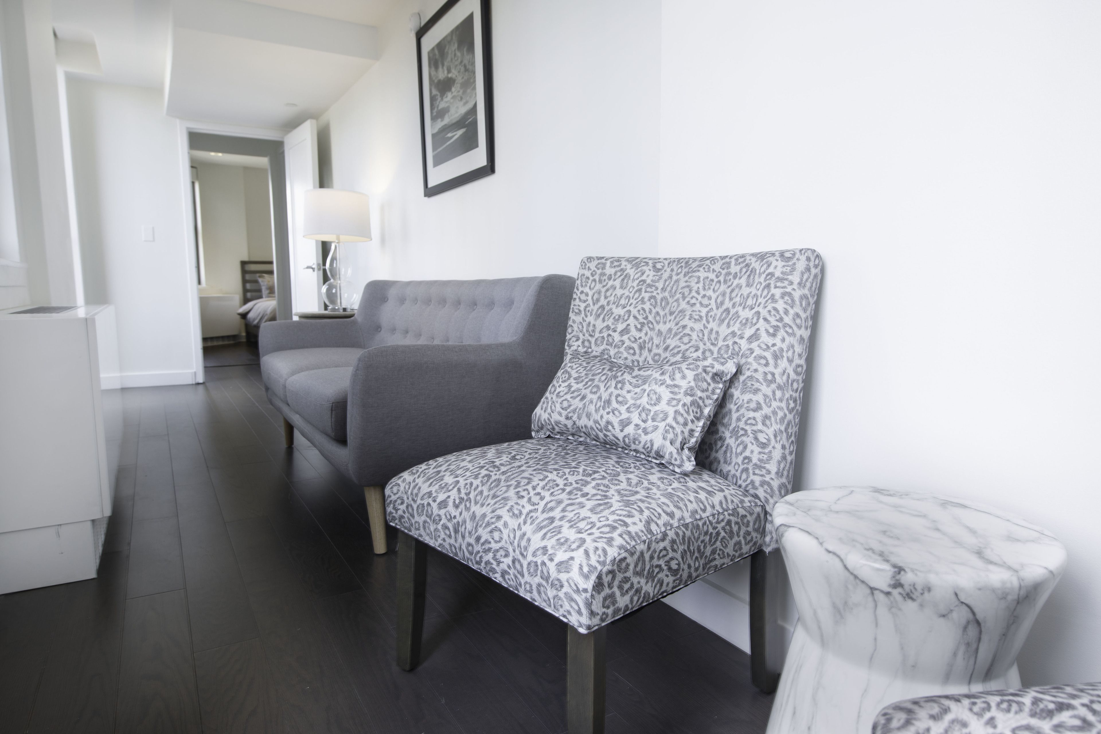 Un salon moderne avec un canapé gris, un fauteuil à motifs et une table d’appoint en marbre.