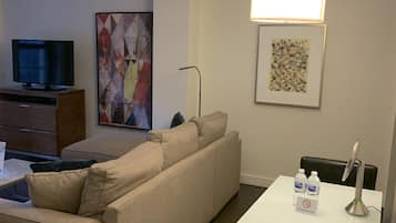 A modern living room with a sofa, a flat-screen TV, a coffee table, and a dining area with a table and chairs.