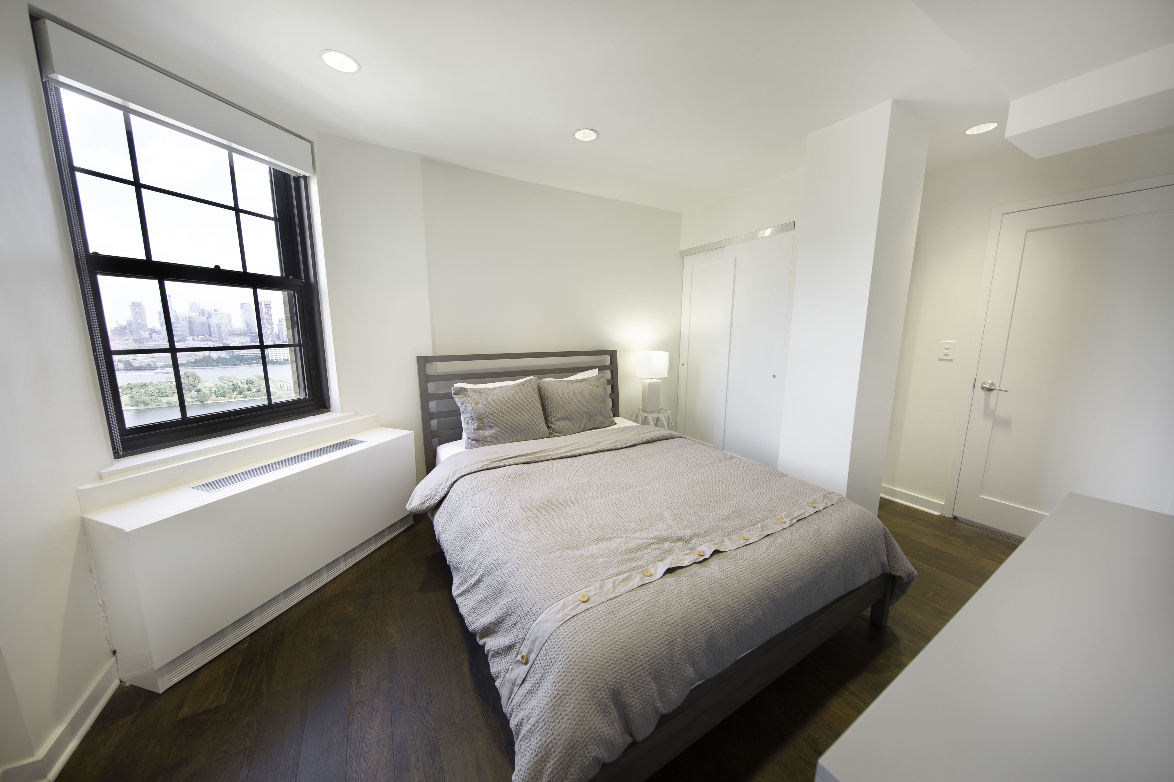 A bedroom with a large window, a bed, a bedside table, and a wardrobe.